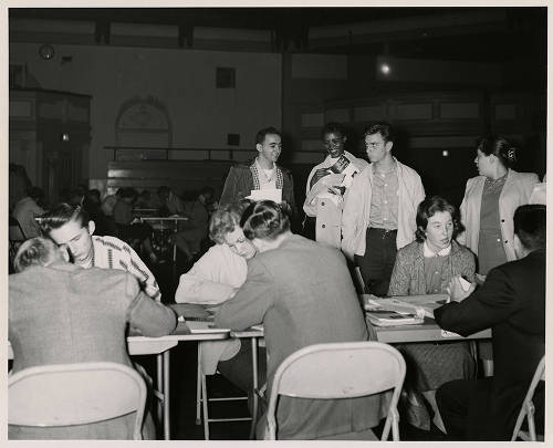 Students sitting at a table and others standing during freshman orientation in 1957. (Image courtesy of DePaul University Special Collections and Archives)